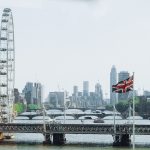 Blick auf die Themse in London und viele Brücken. Im Vordergrund weht eine britische Flagge.
