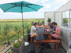 F&uuml;nf Personen sitzen auf der Terrasse des CoWorkLand-Containers. Alle arbeiten an ihren Ger&auml;ten. Im Hintergrund sieht man nichts als Felder.