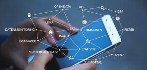 Eine Person bedient ein Smartphone. Man sieht die beiden H&auml;nde und das Smartphone. &Uuml;ber das Display dr&uuml;ber gelegt sind verschiedene Schlagw&ouml;rter, wie z.B. Kommunen, Lizenz, Open Data, die verbunden sind.