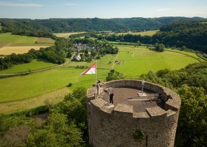 Drohnen-Luftbildaufnahme der Burg Blankenberg in Hennef. Oben auf der Burg ist eine Person,, die an einer der zahlreichen Funkantennen steht.