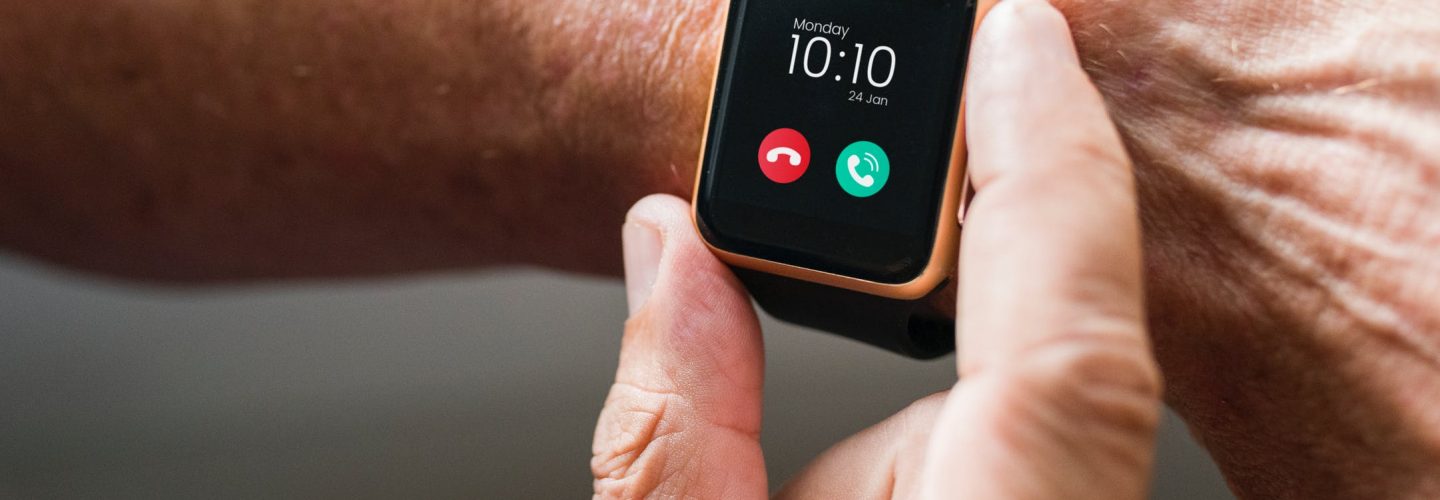 Am linken Arm eines älteren Menschen ist eine Smartwatch. Man sieht, dass ein Anruf auf WhatsApp eingeht. Die rechte Hand der Person fastt mit Daumen und Zeigefinger an die Uhr.