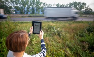 Die Bad Hersfelderin Katja Sippel h&auml;lt ihr Tablet in die Luft und misst mit einer App den Verkehrsl&auml;rm an der A4. Frau Sippel ist in der unteren H&auml;lfte des Bildes, in der oberen H&auml;lfte sind die verschwommenen Konturen eines vorbeifahrenden LKWs.