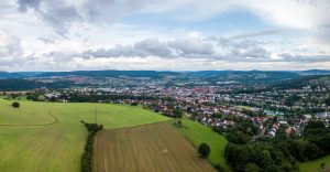 Lauftaufnahme aus einer Drohne. Im Vordergrund sind gr&uuml;ne Wiesen. Weiter am Horizont ist die hessische Mittelstadt Bad Hersfeld.