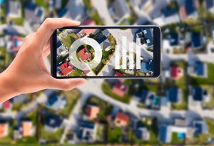 Das Key Visual f&uuml;r den Relaunch des Wegweiser Kommune. Gro&szlig;formatig ist eine Stadt aus der Vogelperspektive zu sehen. Mittig h&auml;lt eine Hand ein Smartphone und auf dme Display sind Diagramme zu sehen.