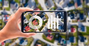 Das Key Visual f&uuml;r den Relaunch des Wegweiser Kommune. Gro&szlig;formatig ist eine Stadt aus der Vogelperspektive zu sehen. Mittig h&auml;lt eine Hand ein Smartphone und auf dme Display sind Diagramme zu sehen.